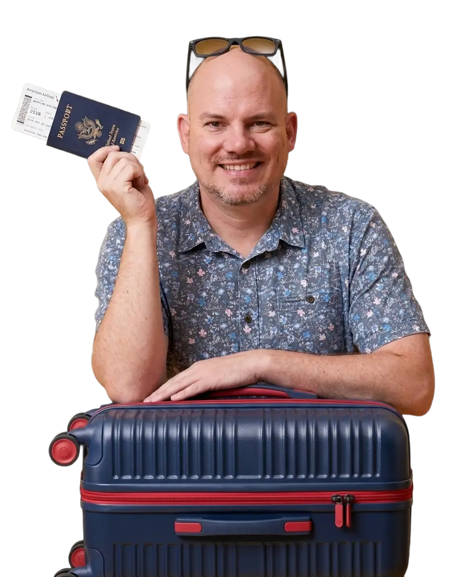 Smiling man with shaved head and beard, wearing blue floral short-sleeved shirt, leaning on navy blue suitcase, holding blue US passport and American Airlines boarding pass.